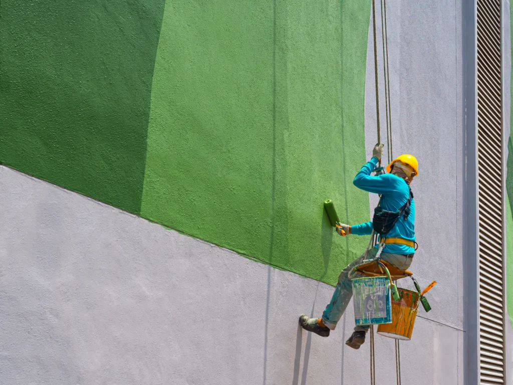 Man doing painting services on a building while suspended in the air.