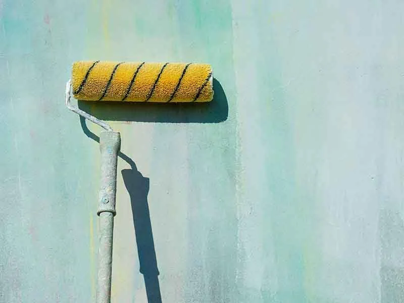 Paint roller painting a wall light green.