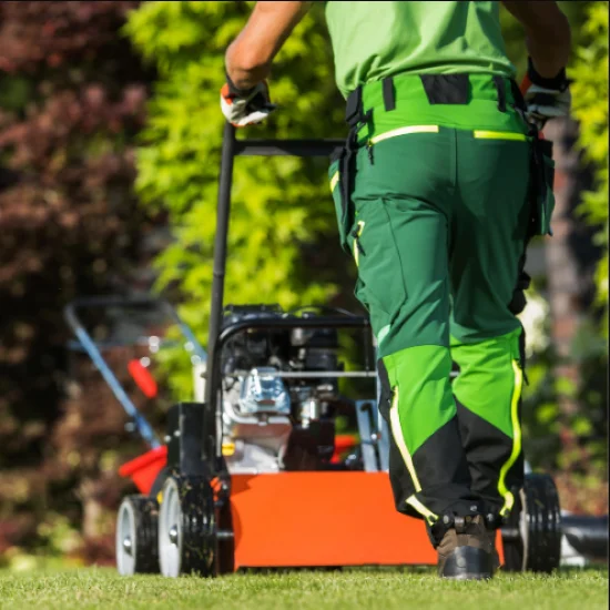 Gardener wearing green and mowing a lawn with a lawnmower.