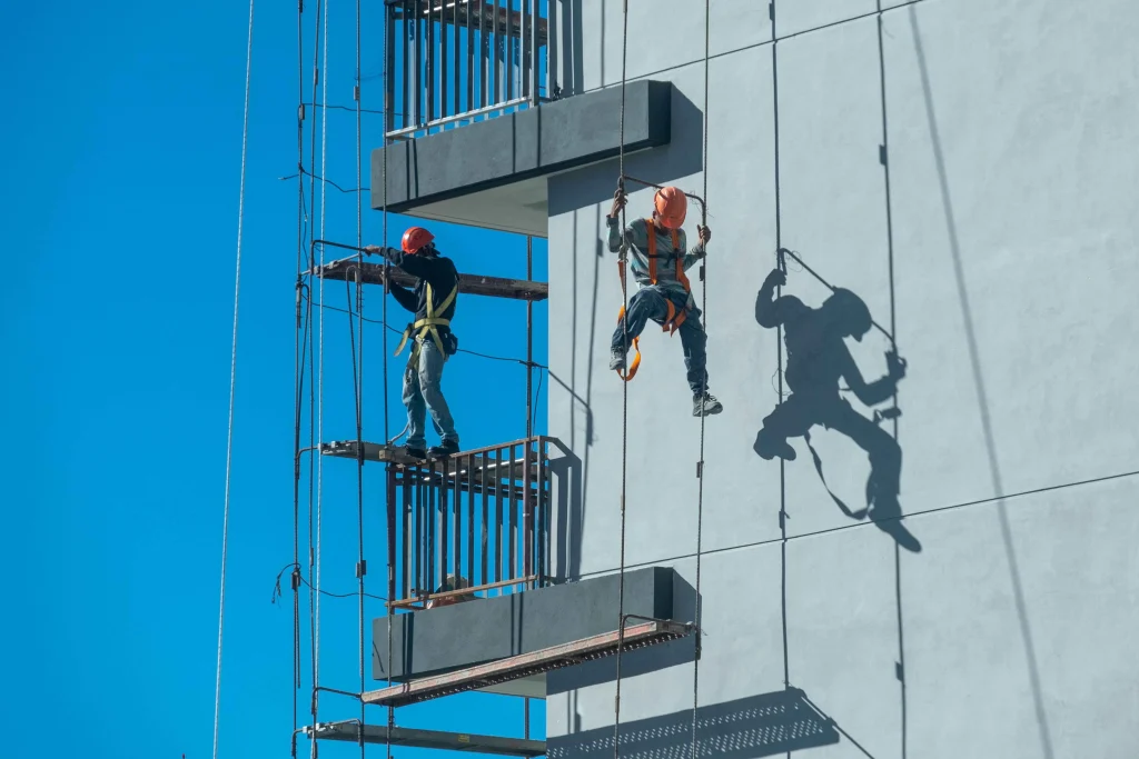 2 workers climbing the side of a building and doing their work.