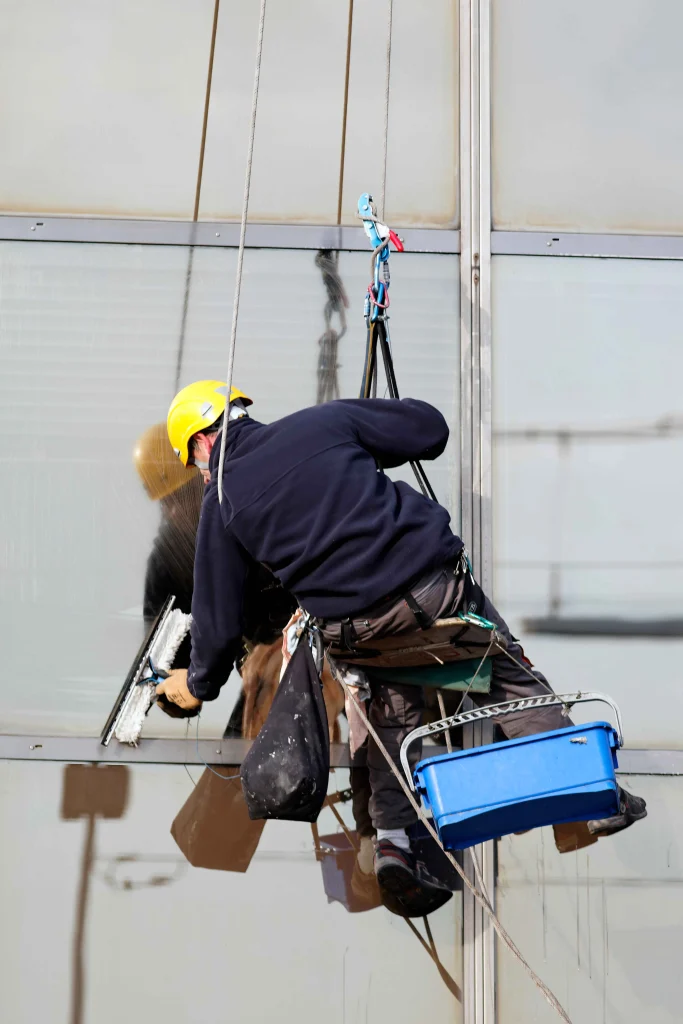 Window cleaner sitting on a suspended seat and wiping the window of a building.