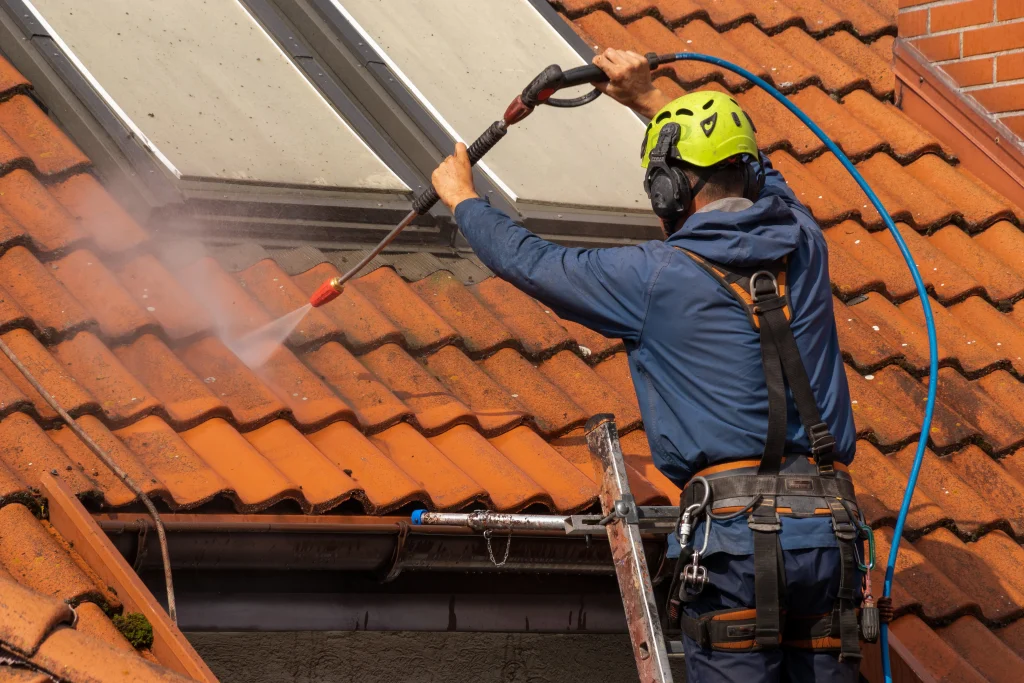 Man pressure washing a roof while standing on a ladder.