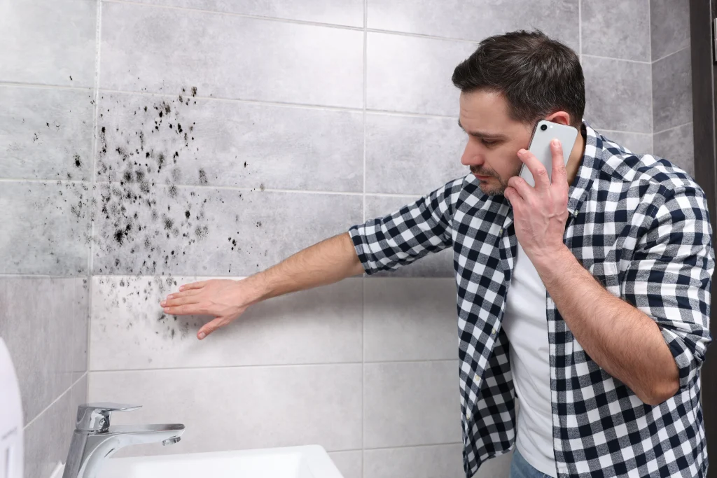 Man on the phone with a mold removal company while inspecting the black mold in his bathroom.