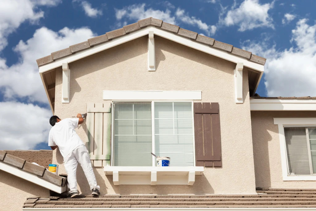 Man painting his house exterior while standing on the roof.