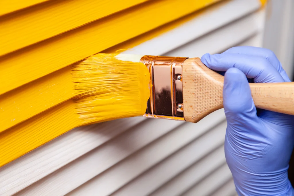 Person painting house yellow after finding out how to paint a house exterior.