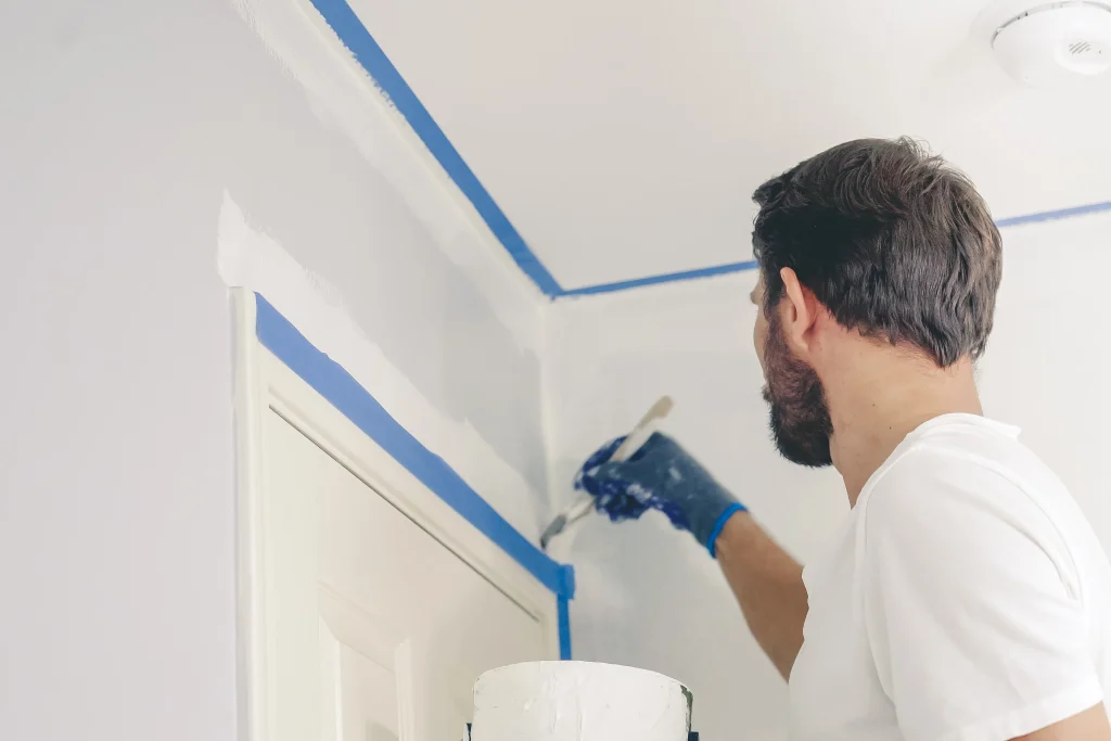 Man painting a house interior using masking tape and paint.