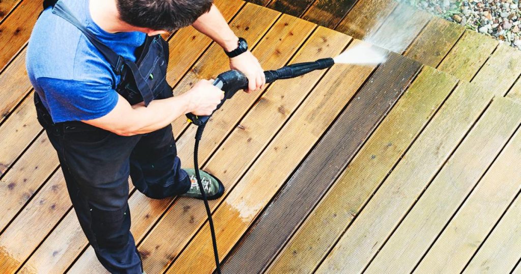 Professional deck cleaner using high-pressure washing equipment to clean a wooden deck effectively.