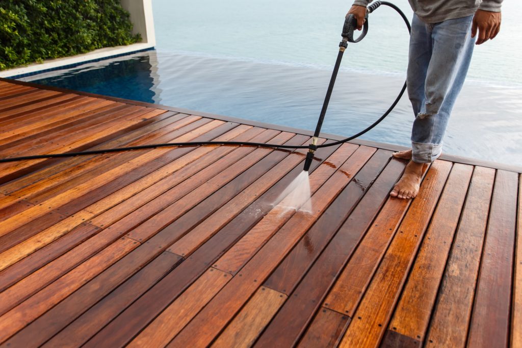 Professional using a high-pressure washer to clean a wooden deck, removing dirt and grime effectively.