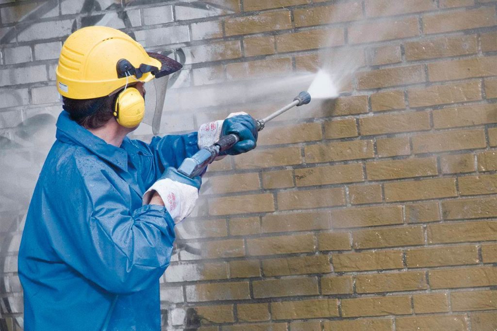 Graffiti removal expert in Melbourne using high-pressure cleaning on a brick wall.