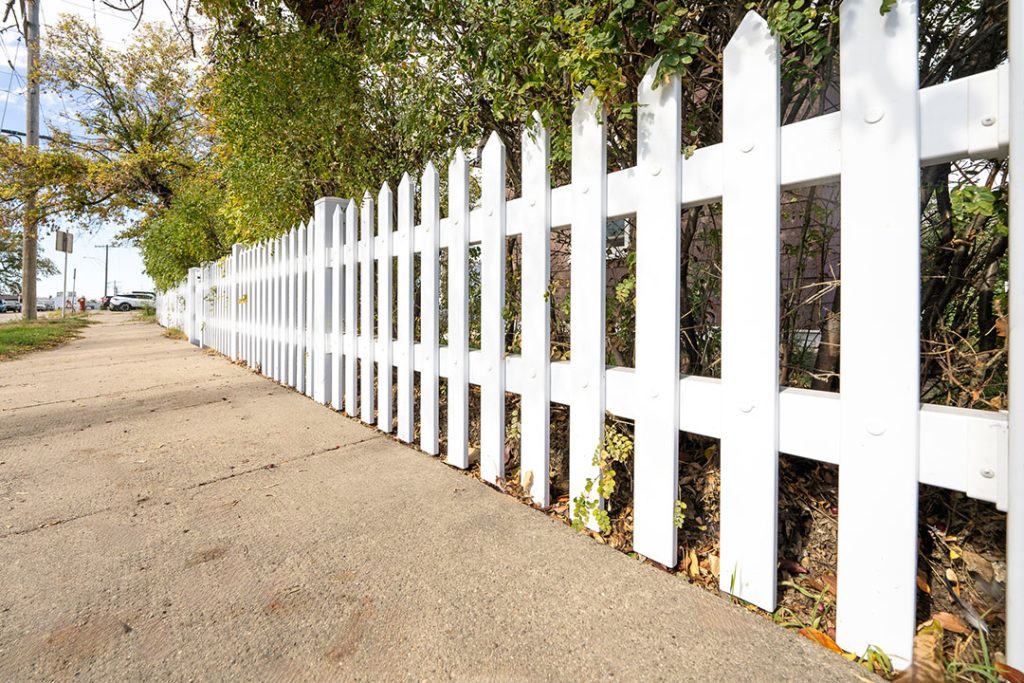 Pristine white picket fence along a sidewalk, showcasing the results of professional fence cleaning services in Melbourne.