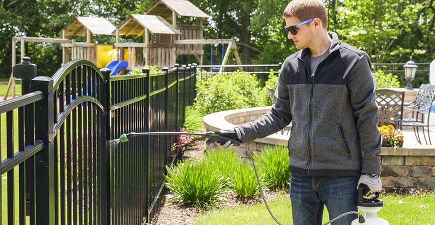 Worker cleaning a metal fence in a backyard with professional fence cleaning services in Melbourne.