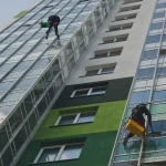 Worker using a high-powered washer to clean a stained driveway Full Building Exterior Cleaned