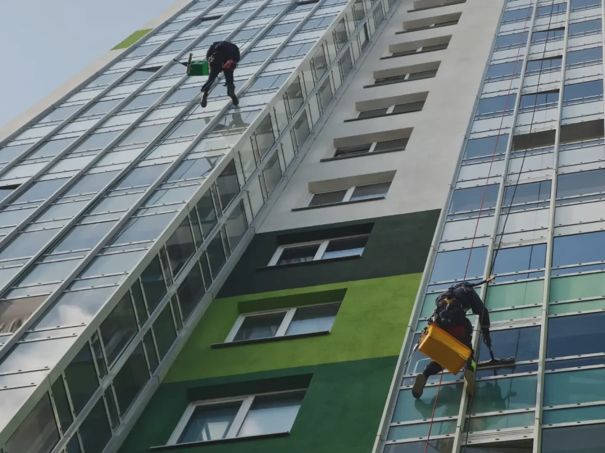 Window cleaners working on cleaning the windows of a building while sitting on suspended seats.