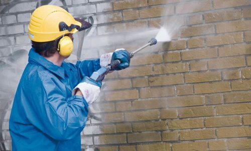 Graffiti removal expert in Melbourne using high-pressure cleaning on a brick wall.