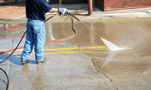 Worker using high-pressure water jet to clean a car park in Melbourne